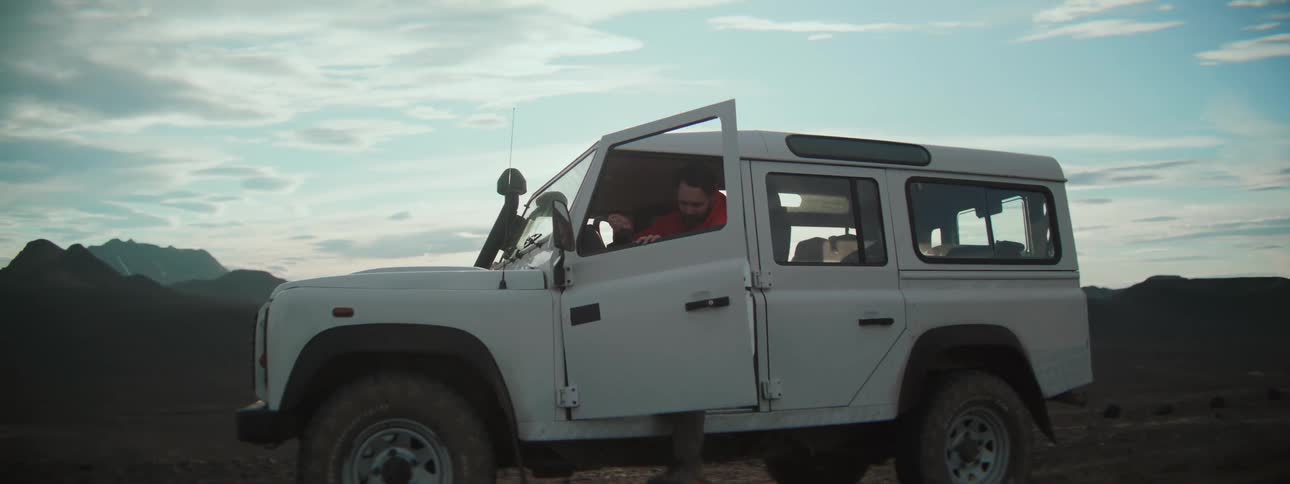 A rugged explorer steps out of his white SUV into the barren wilderness as the sun shines brightly