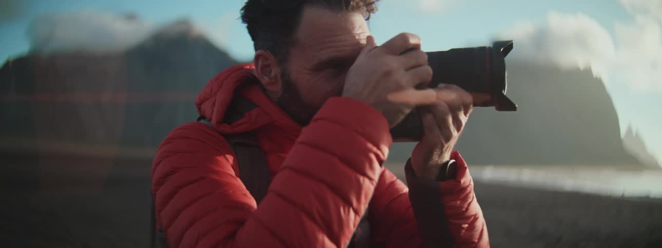 A focused photographer in a red jacket captures the beauty of a dramatic mountain landscape during golden hour