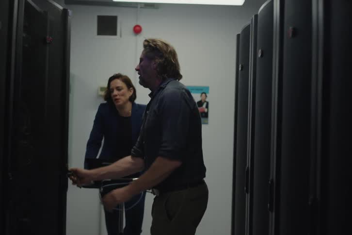 A male IT technician explains the system to his female colleague before opening a server rack in a cold data center