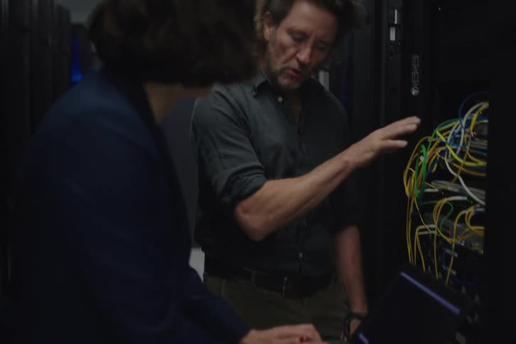 An IT engineer and his colleague collaborate to troubleshoot a network issue in a dark server room