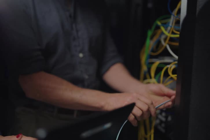 Close-up of IT professionals disconnecting a network cable from a laptop and plugging it into a server rack in a data center