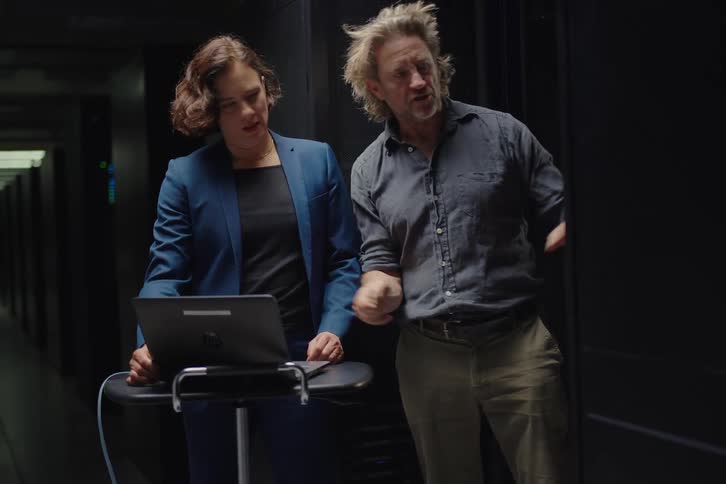 A male and female IT professional collaborate on a laptop while troubleshooting in a modern server room