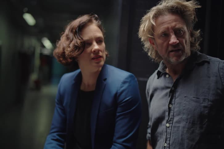 A male and female technician work together on a laptop in a dimly lit server room corridor