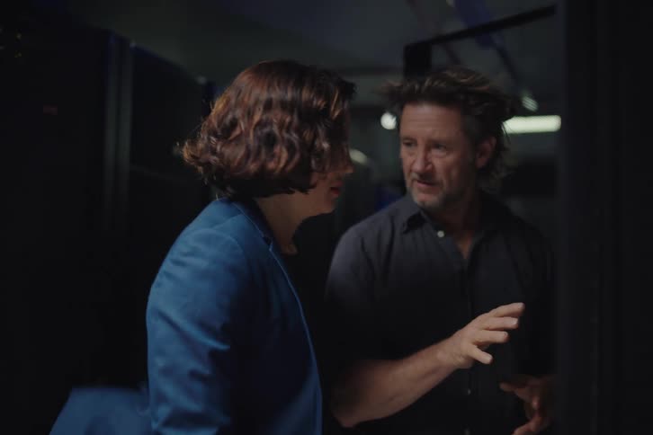 Two IT professionals, a man and a woman, discuss server rack wiring and configurations in a dark data center
