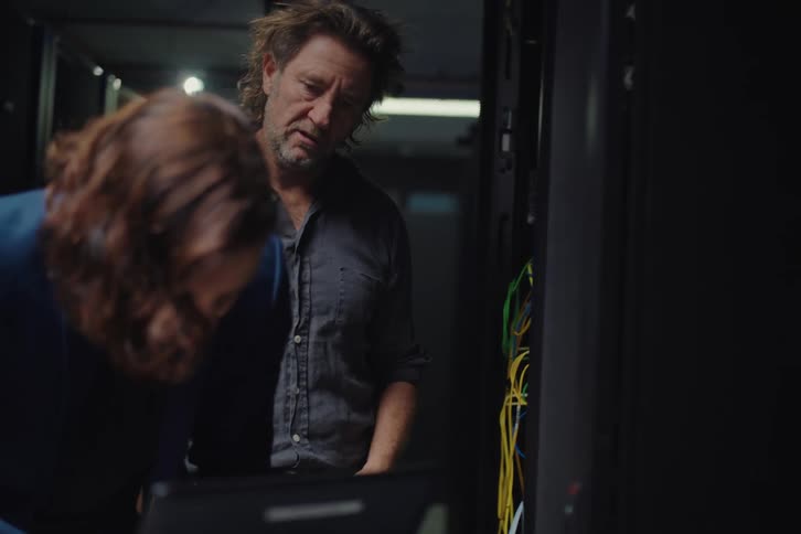 Two IT professionals, a man and woman, collaborate while working on a server rack with a laptop in a data center