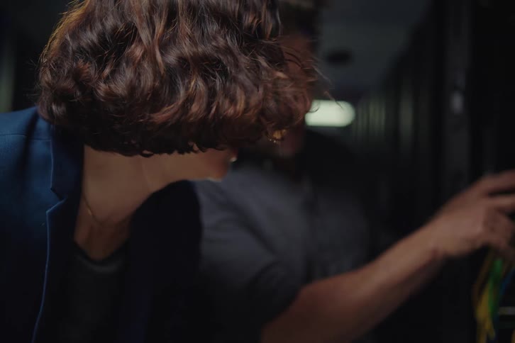 Male and female IT technicians collaborate on a network issue in a server room, with the man inspecting cables while the woman types on a laptop