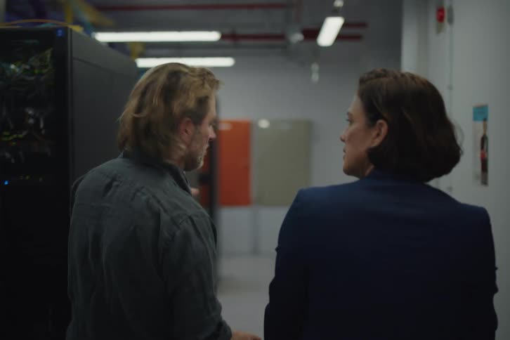 A male IT specialist and a businesswoman walk through a server room corridor while discussing the data racks