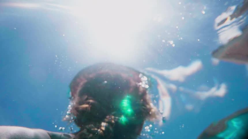 A female swimming in a pool floats to the surface under the bright sun