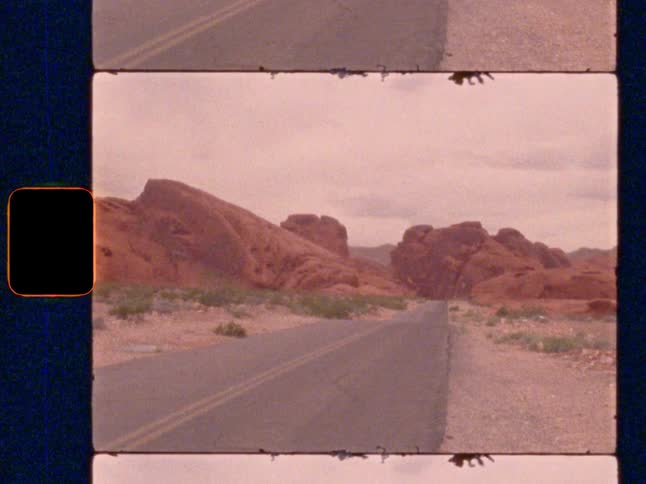 An empty desert road winding through large red rock formations, on Super 8 film