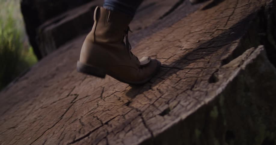 Close-up in slow motion of a person's hiking boots carefully walking up a steep, textured rock formation