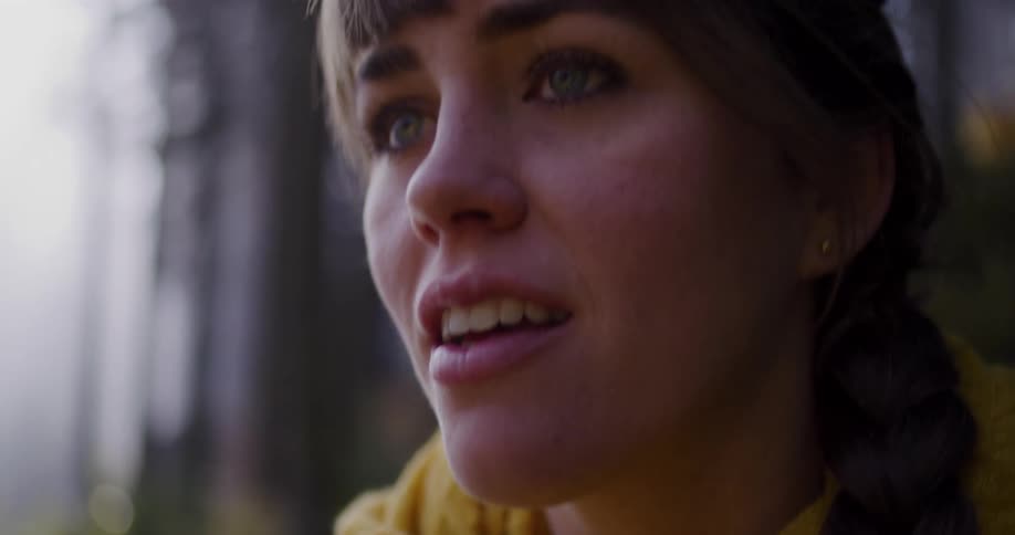 An intimate slow-motion close-up of a young woman's face as she breaks into a gentle smile while in a peaceful forest