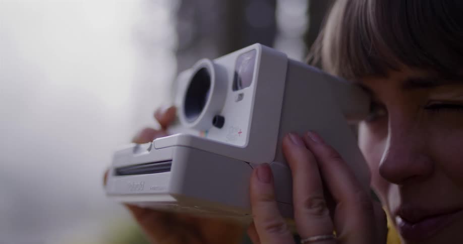 A woman in a yellow scarf takes a picture with a vintage-style instant camera in slow motion