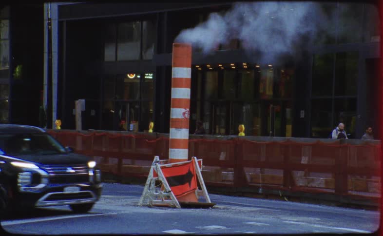 Gritty Super 8 footage captures an iconic New York City steam pipe venting on a busy street as traffic passes by