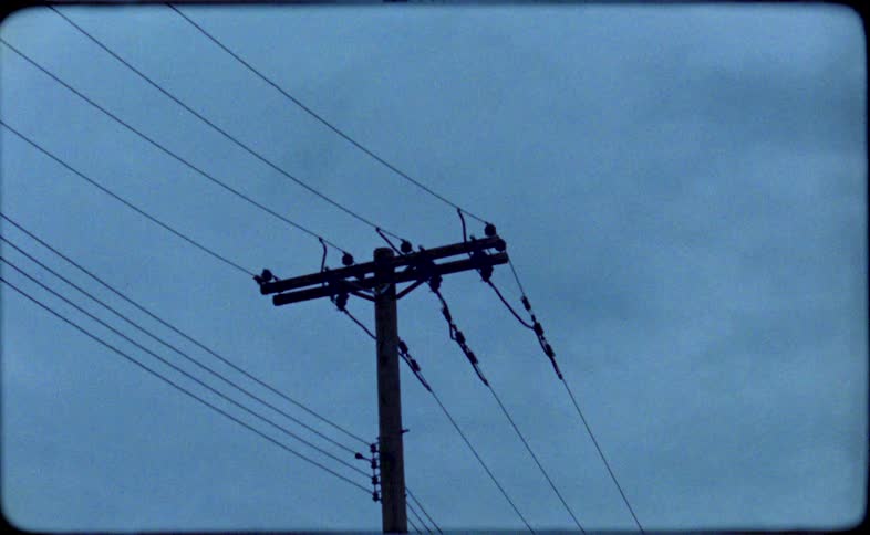 A low-angle, vintage Super 8 film shot of a silhouetted telephone pole against a dark and gloomy sky