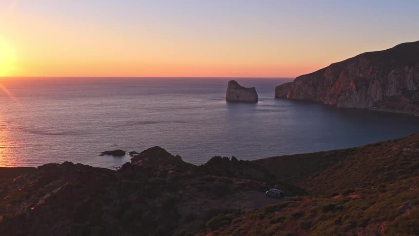 A stunning timelapse captures the sunrise over a tranquil bay, illuminating a majestic sea stack and rugged cliffs