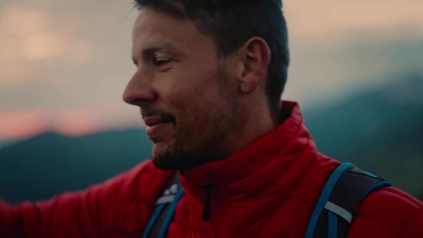A male climber in a red jacket removes his helmet to enjoy the scenic mountain view at sunset