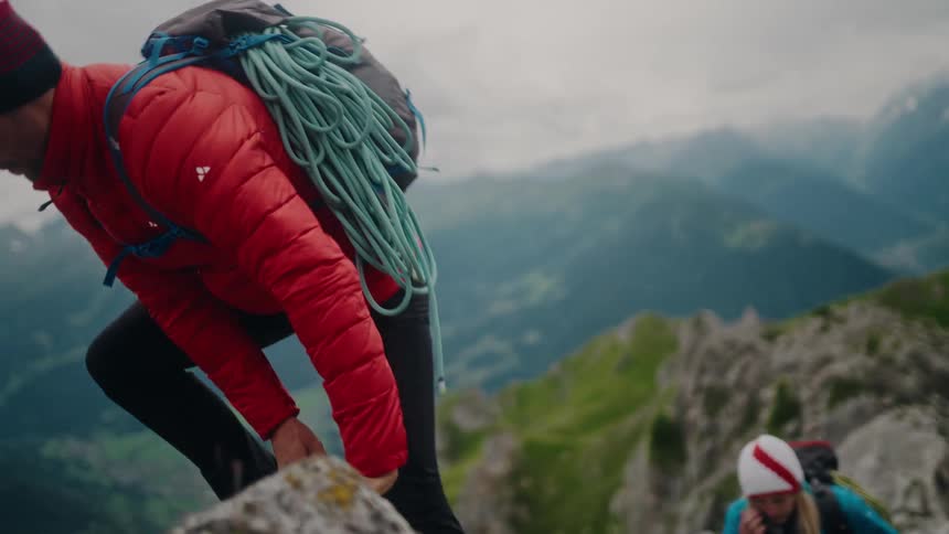 A male mountaineer offers a helping hand to his female partner as they carefully ascend a steep and rocky mountain trail