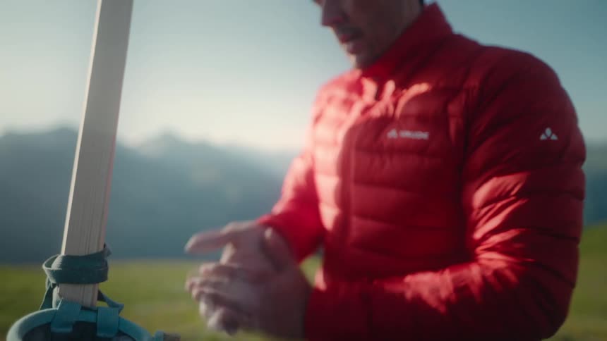 A male climber in a red jacket applies chalk to his hands in slow motion before training on a hangboard in the mountains