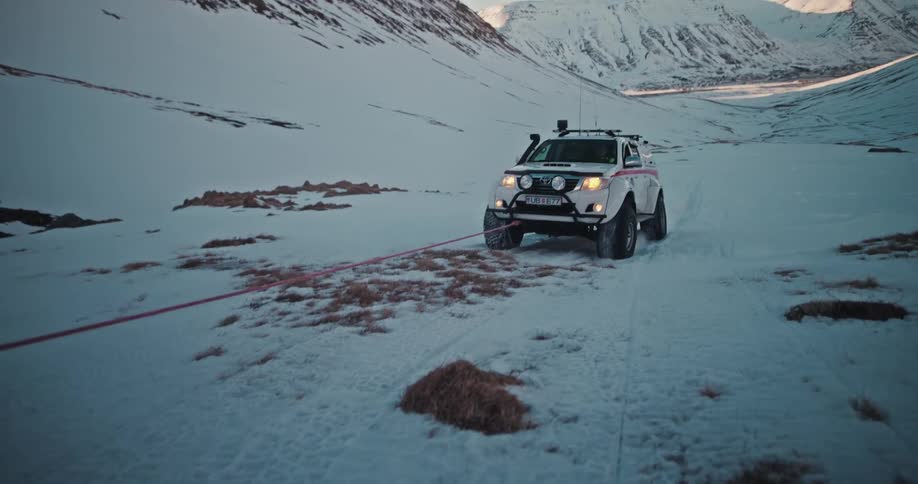 An Icelandic search and rescue vehicle tows another 4x4 through a snowy mountain landscape