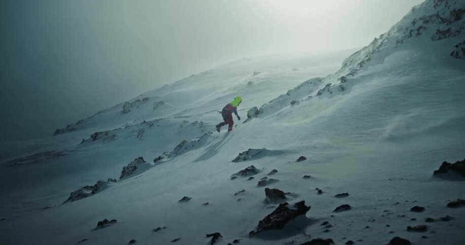 A lone mountaineer in bright gear braves a fierce blizzard while ascending a steep, snow-covered slope in slow motion