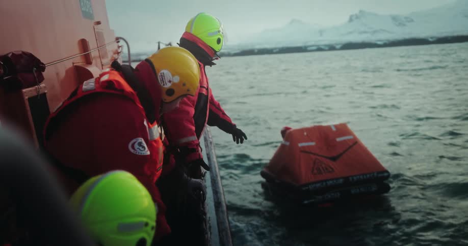 A maritime rescue team observes a life raft from their boat during a safety mission in cold, arctic waters