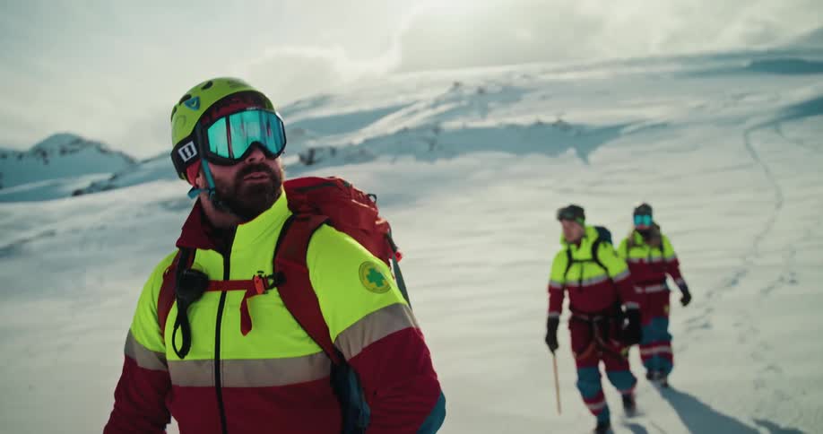 Cinematic slow motion of a focused mountain rescue team trekking through a vast, snow-covered alpine environment