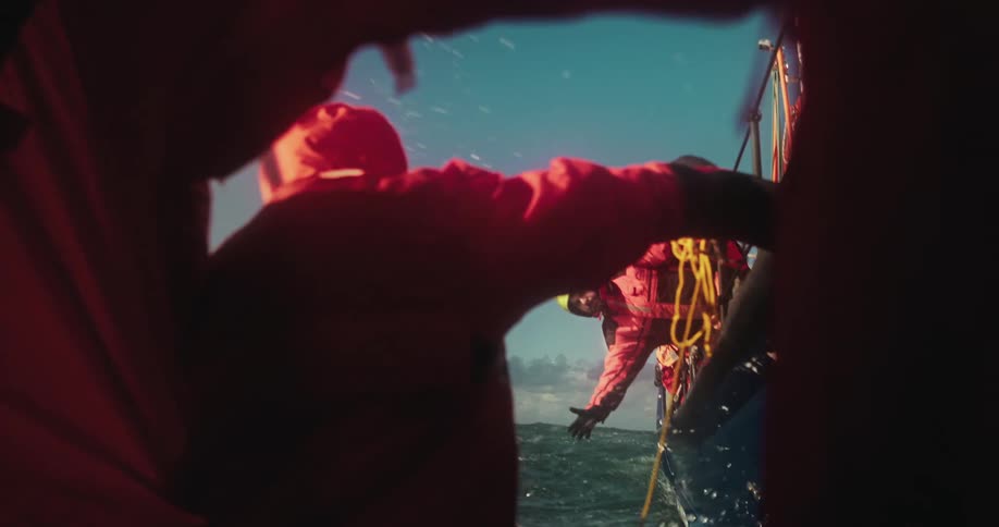 A dramatic first-person perspective in slow motion of a person being rescued from a life raft by a team on a boat in the open ocean