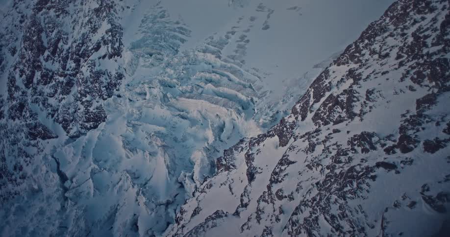 A slow aerial reveal of a vast, frozen glacier wedged between rugged, snow-covered mountain peaks