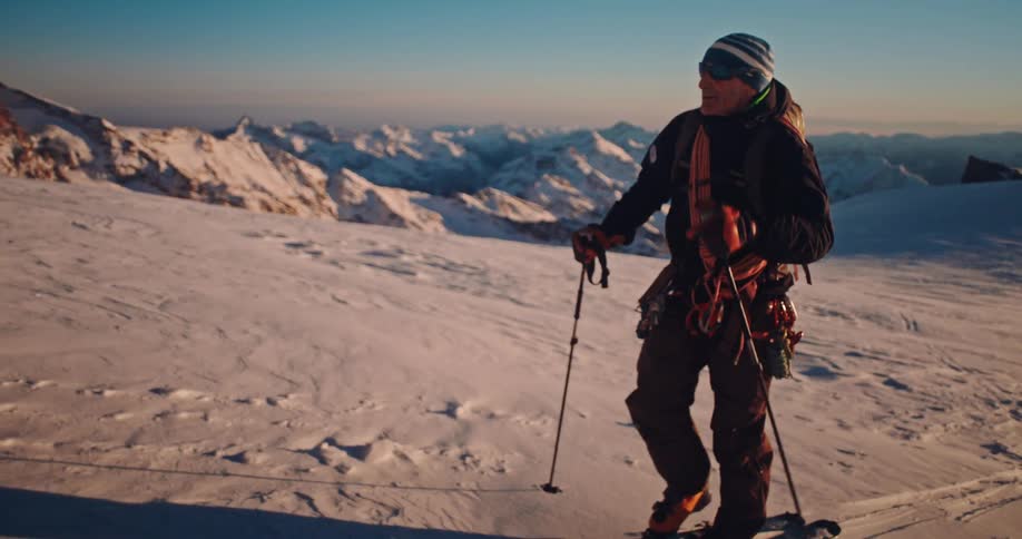 A mountaineer on skis traverses a snowy mountain slope with a stunning view of the surrounding peaks at sunrise