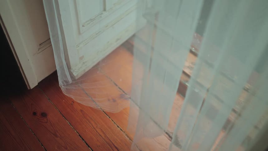 A delicate white sheer curtain billows gently in the breeze over a warm wooden floor