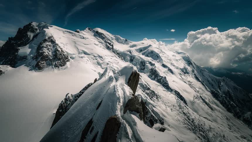 A breathtaking timelapse captures the majestic, snow-covered peaks of Mont Blanc against a deep blue sky with rolling clouds