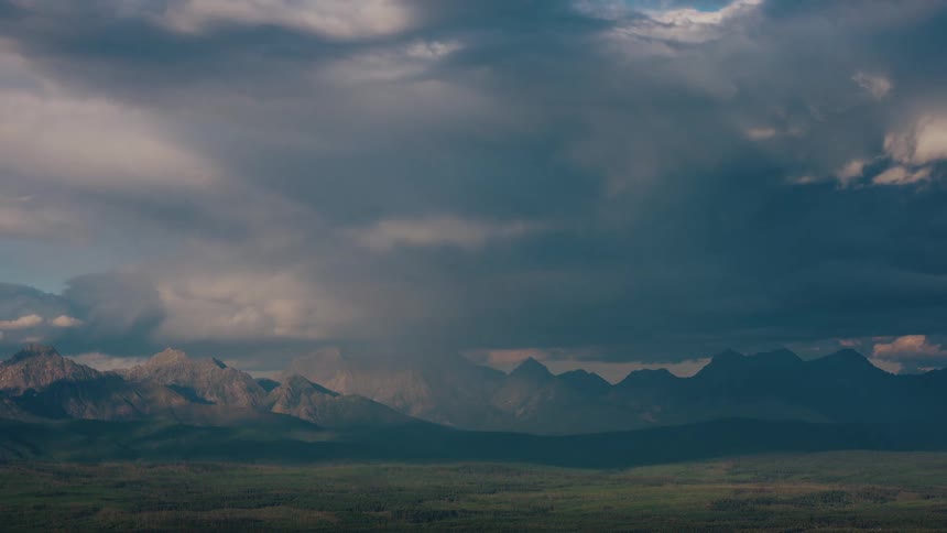 Heavy storm clouds drift slowly above a majestic mountain range and lush green valley