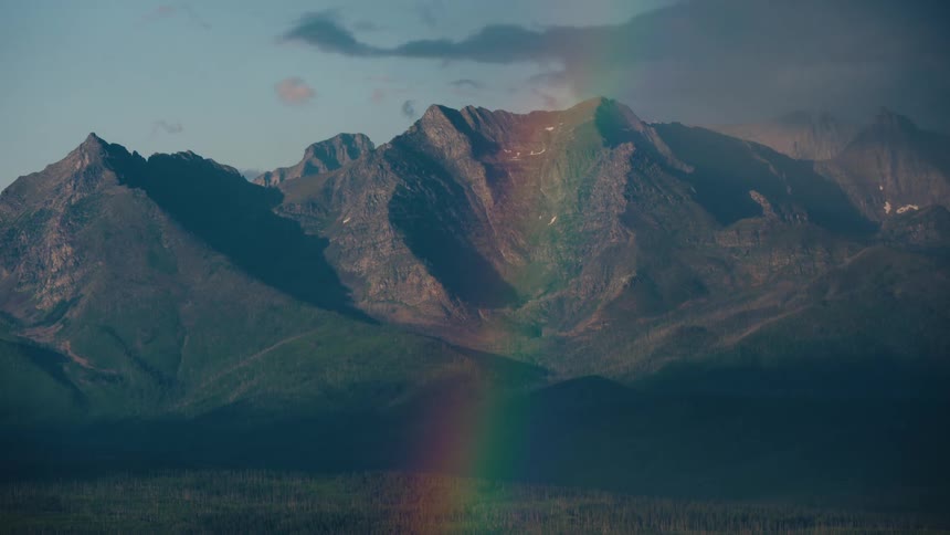 A stunning, vibrant rainbow graces the face of a rugged mountain range under a calm sky