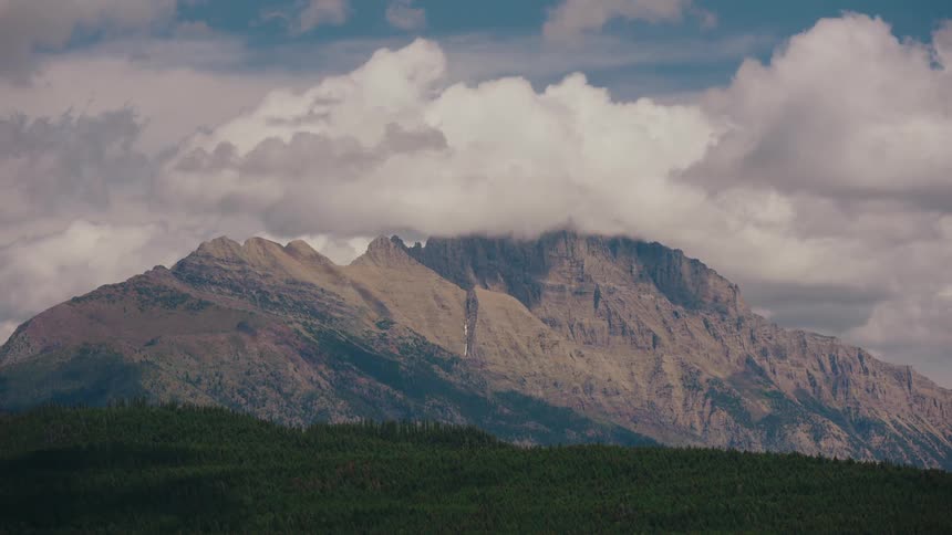 A time-lapse of clouds and shadows sweeping across a majestic mountain range above a dense green forest