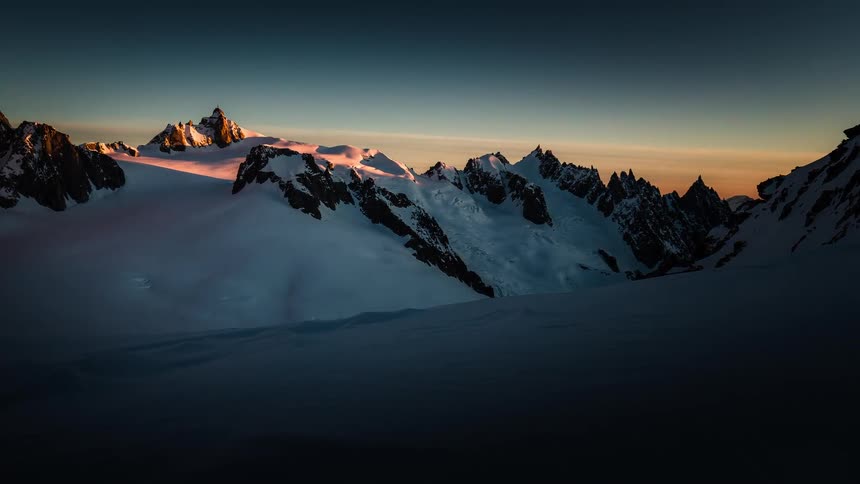 A beautiful timelapse shows the sun rising over a majestic, snow-covered mountain range, casting golden light on the peaks and valleys