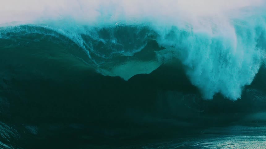 A massive turquoise ocean wave builds and crashes in dramatic slow motion