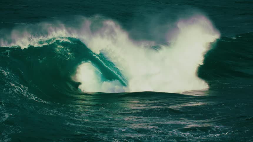 A surfer gets wiped out by a massive, powerful ocean wave breaking in dramatic slow motion