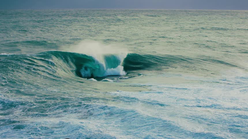 A massive teal ocean wave curls and crashes in dramatic slow motion