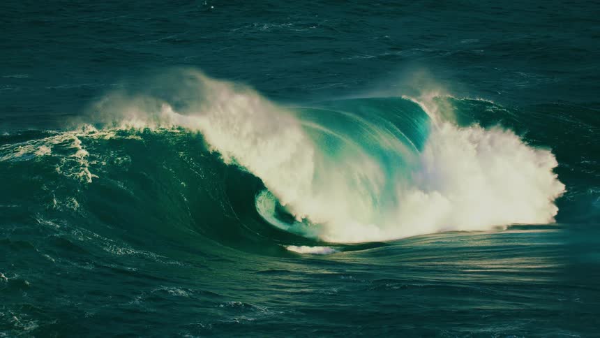 An enormous, powerful ocean wave builds and crashes in dramatic slow motion, creating a perfect barrel