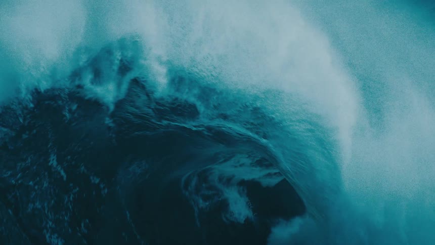 An immense ocean wave curls and crashes in dramatic, powerful slow motion