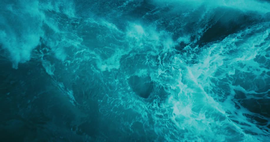 Close up view of a mesmerizingly large turquoise ocean wave cresting and breaking in slow motion