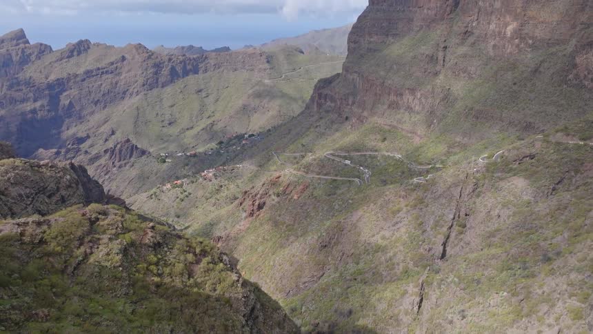 A slow tilt up reveals the stunning Masca Valley in Tenerife, with its winding road, remote village, and the vast ocean in the distance
