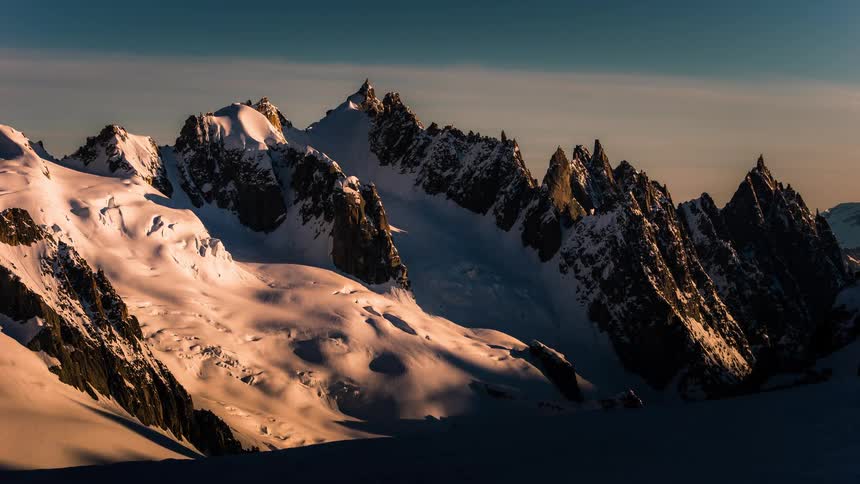 Majestic time-lapse of sunrise casting a warm golden light across a rugged snow-capped mountain range