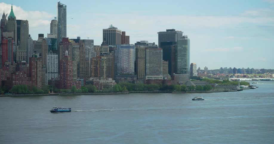 Boats sail on the river with the impressive New York City skyline of Lower Manhattan in the background on a clear day
