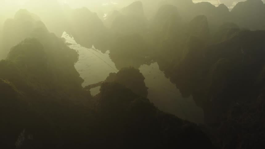 Sunlight filters through thick mist over a serene bay nestled among lush, green mountains