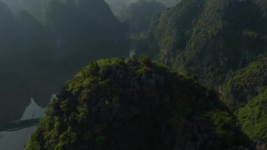 A slow aerial pullback reveals a stunning panoramic view of lush green karst mountains and a serene river valley in Vietnam