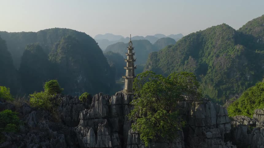 A majestic stone pagoda stands watch over a vast, hazy landscape of jungle-covered karst mountains in Vietnam