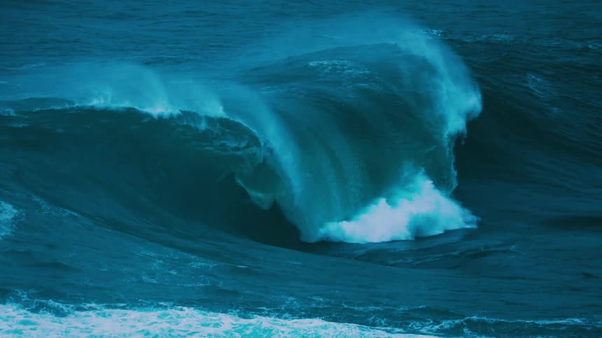 A massive, powerful turquoise ocean wave forms and breaks in dramatic super slow motion