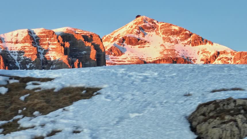 A slow tracking shot across a snowy landscape reveals the majestic sunlit peaks of a mountain range at sunrise