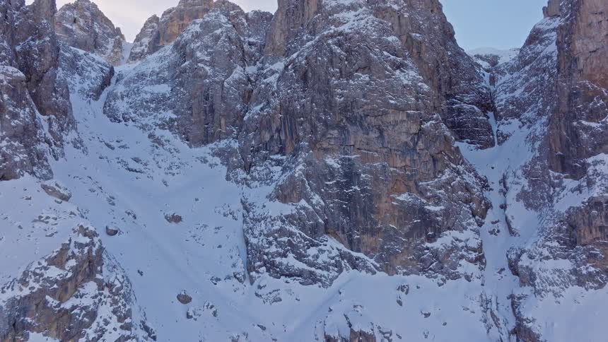 A dramatic aerial shot slowly pulls back to reveal the immense and rugged peaks of a snow-covered mountain range